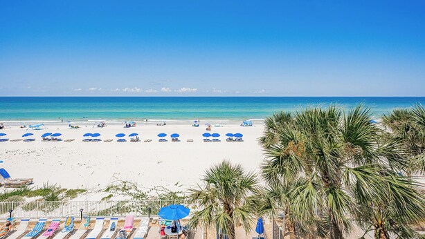 Una playa de arena blanca, sombrillas azules y palmeras.