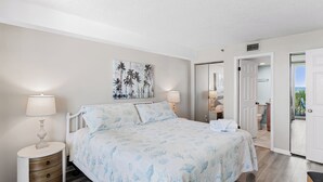 Een slaapkamer met een bed, twee nachtkastjes, een schilderij en een deur naar een balkon.