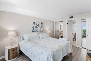 Een slaapkamer met een bed, twee nachtkastjes, een schilderij en een deur naar een balkon.