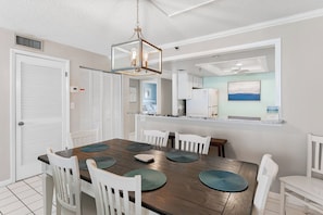 Un espace repas avec une table en bois, des chaises blanches et un luminaire suspendu.