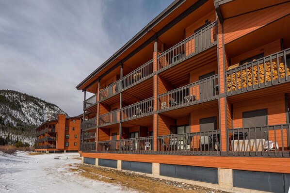 A multi-story hotel with balconies, wooden exterior, and a view of snow-covered mountains.