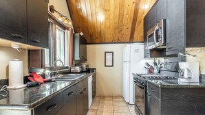 Une cuisine de taille réduite, avec des meubles de couleur sombre, un réfrigérateur en acier inoxydable, un four à micro-ondes, une cuisinière et un évier.