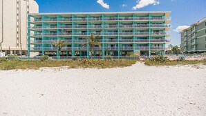Un hotel de varios pisos con balcones, situado en una playa de arena con palmeras.