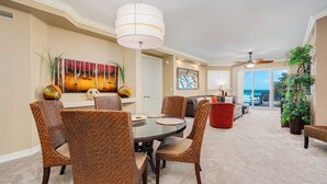 A spacious living area with a dining table, wicker chairs, a red sofa, and a large window offering a view of the ocean.