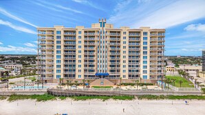A multi-story hotel with a central courtyard, a swimming pool, and a beach area.