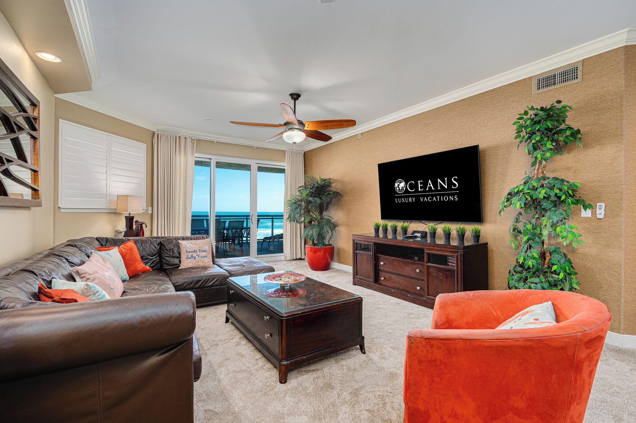 A living room with a brown leather sofa, a red armchair, a wooden coffee table, and a television on the wall.