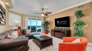 A living room with a brown leather sofa, a red armchair, a wooden coffee table, and a television on the wall.