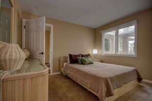 Un dormitorio con cama, mesitas de noche, lámpara, puerta y ventana.