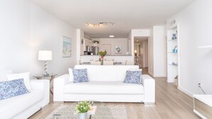 A modern living room with a white sofa, a glass coffee table, and a kitchen in the background. - Bright condo with amazing bay views. WIFI + Parking (Sunny Isles Beach)