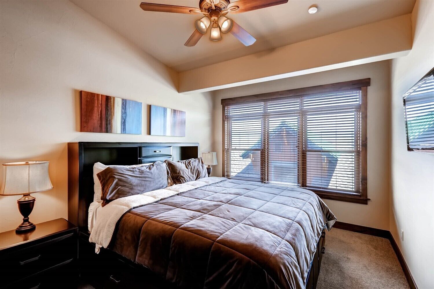 Ein Schlafzimmer mit Bett, Deckenventilator, Nachttisch, Lampe und Fenster mit Jalousien.