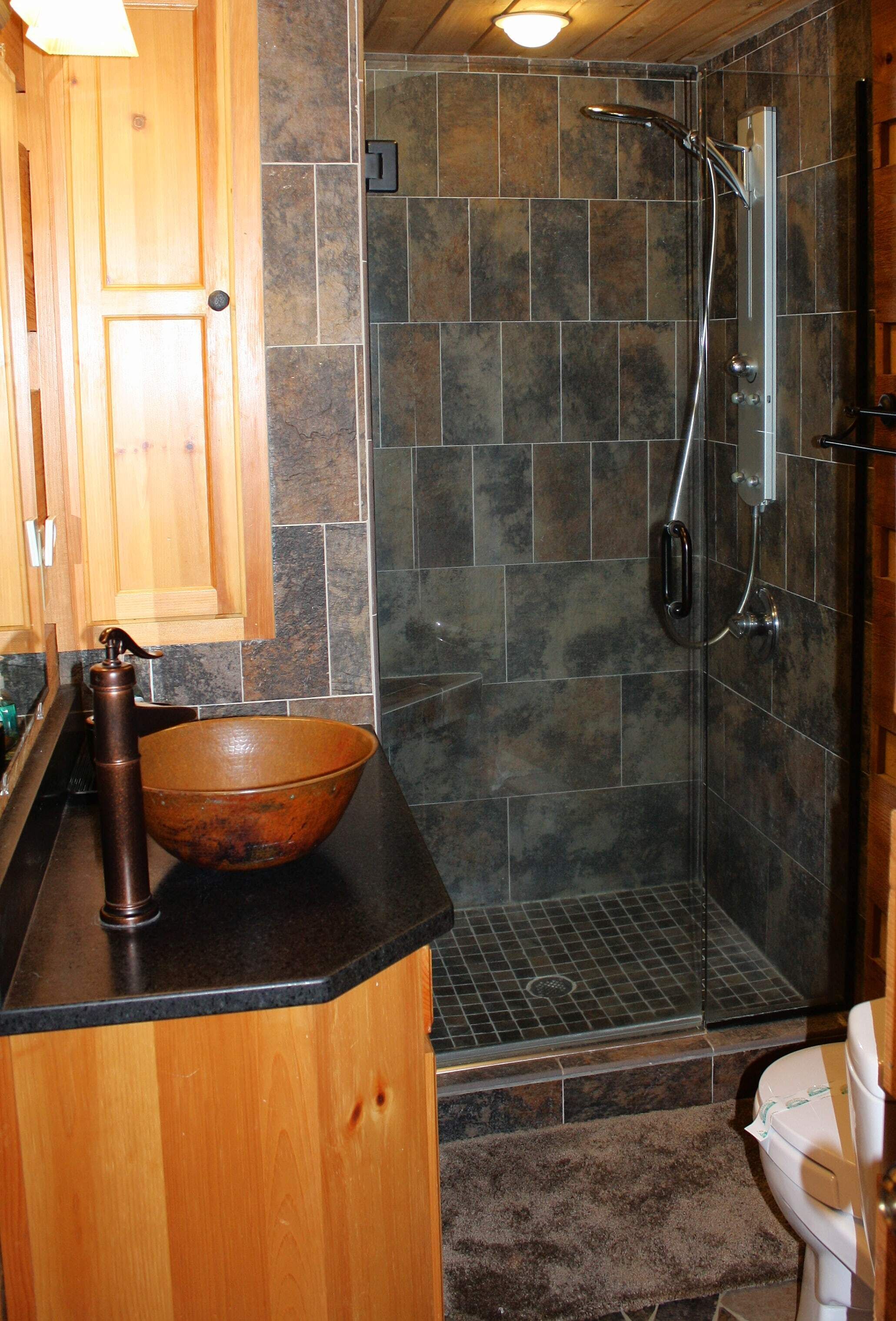 A bathroom with a wooden vanity, a large ceramic sink, a shower with a glass door, and a toilet.