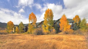 A row of two-story buildings with a grassy field in front, surrounded by trees with autumn foliage. - One bedroom plus loft in Frisco, has three full bathrooms! Plenty of space to relax! (Frisco)