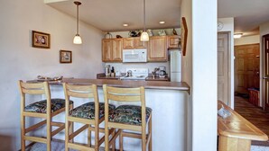 A kitchen with wooden cabinets, a microwave, and a stove. There are three wooden chairs with patterned cushions. - One bedroom plus loft in Frisco, has three full bathrooms! Plenty of space to relax! (Frisco)