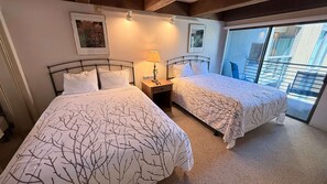A hotel room with two beds, a nightstand with a lamp, and a balcony with a railing.
