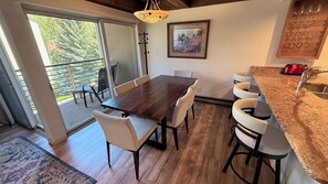 Uma sala de jantar com mesa e cadeiras de madeira, uma cozinha com bancada de granito e uma porta de vidro deslizante que dá para um pátio externo.