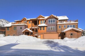 Un grand chalet en bois à plusieurs étages, avec un toit enneigé, de nombreux balcons et un garage.