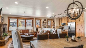 Un salón comedor espacioso con chimenea, una zona de comedor con mesa de madera y una cocina con alacenas de madera y un refrigerador de acero inoxidable.