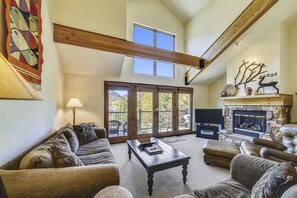 A spacious living room with a high ceiling, a fireplace, and a large sliding glass door leading to an outdoor deck. - Beautiful, modern condo in Marina Park in Frisco. 3 bedrooms, large, open kitchen and private 2 car garage. (Frisco)