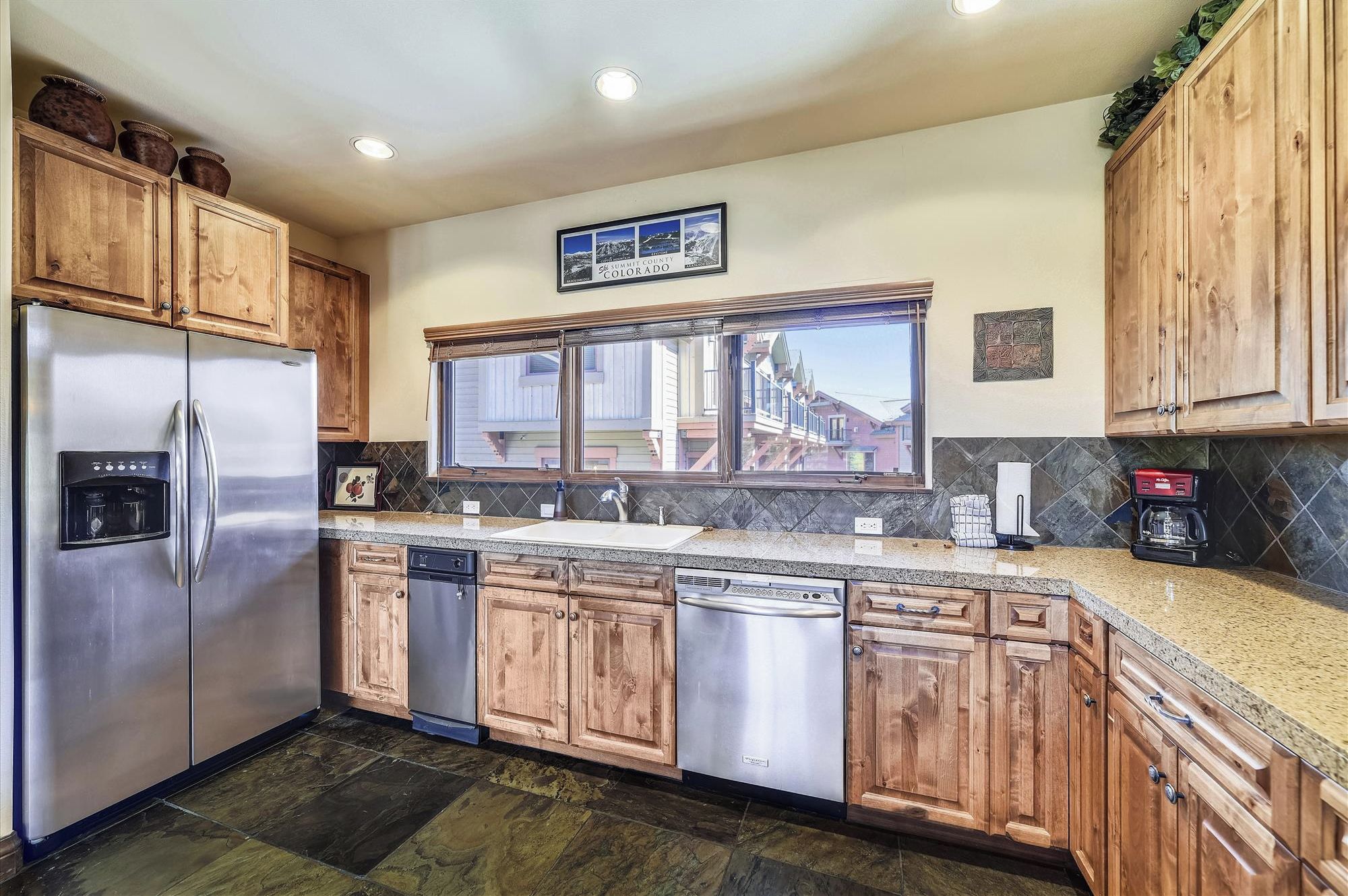 A kitchen with wooden cabinets, stainless steel appliances, a window with a view, and a sign on the wall.