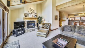 A spacious living room with a stone fireplace, leather armchair, and a sofa. A television and a coffee table with books are also visible. - Beautiful, modern condo in Marina Park in Frisco. 3 bedrooms, large, open kitchen and private 2 car garage. (Frisco)