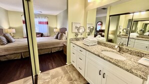 A hotel room with a bed, a bathroom with a sink and mirror, and a window with curtains. - Cheerful, sunny, and spacious, this condo is sure to be a hit with the entire family! (Saint Augustine)