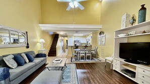 A living room with a sofa, coffee table, TV, and a staircase leading to a kitchen. - Cheerful, sunny, and spacious, this condo is sure to be a hit with the entire family! (Saint Augustine)