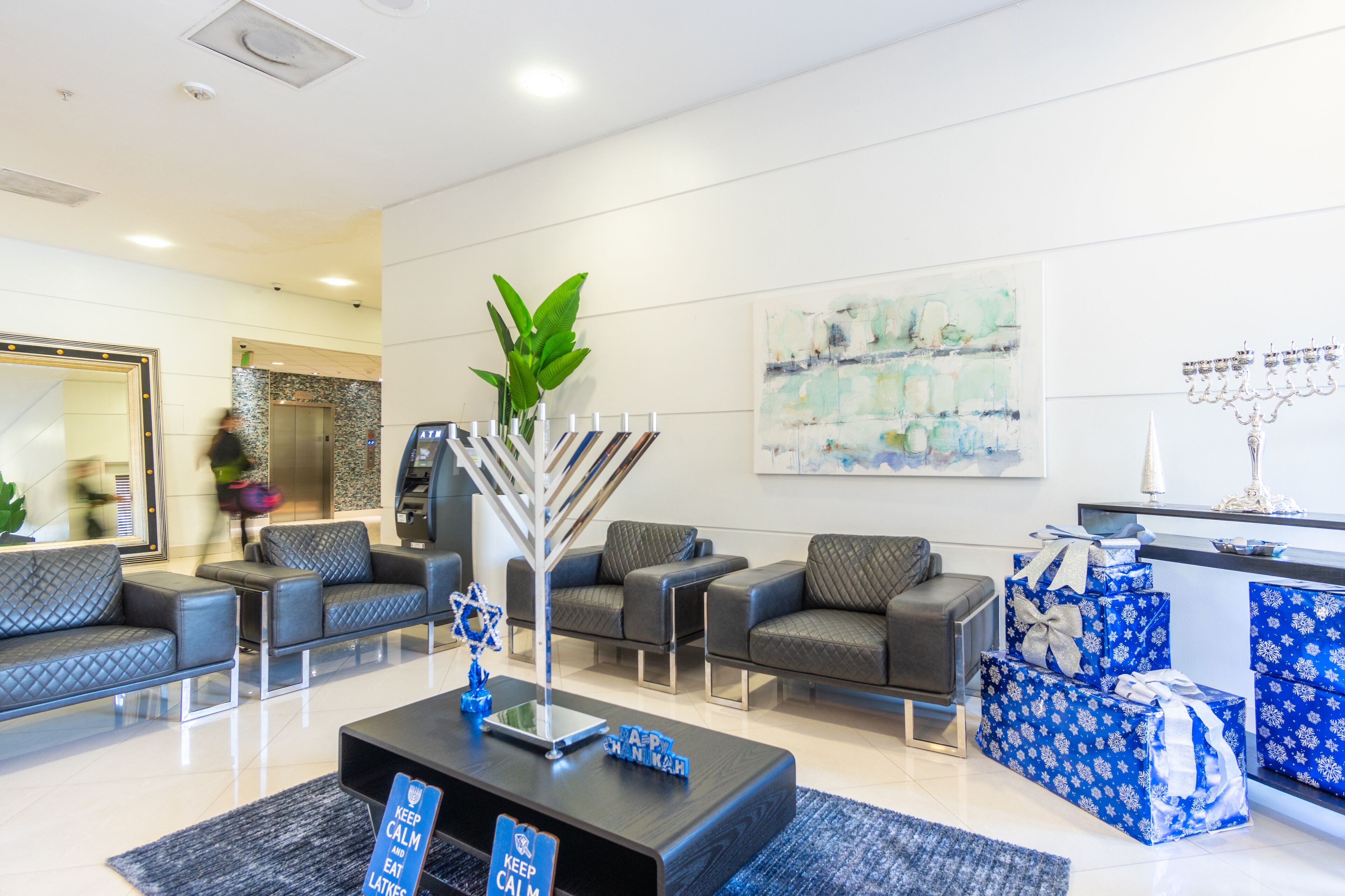 Un hall d’entrée moderne avec des canapés gris à revêtement en tissu, une table basse agrémentée d’une plante décorative et un chandelier à neuf branches fixé au mur.