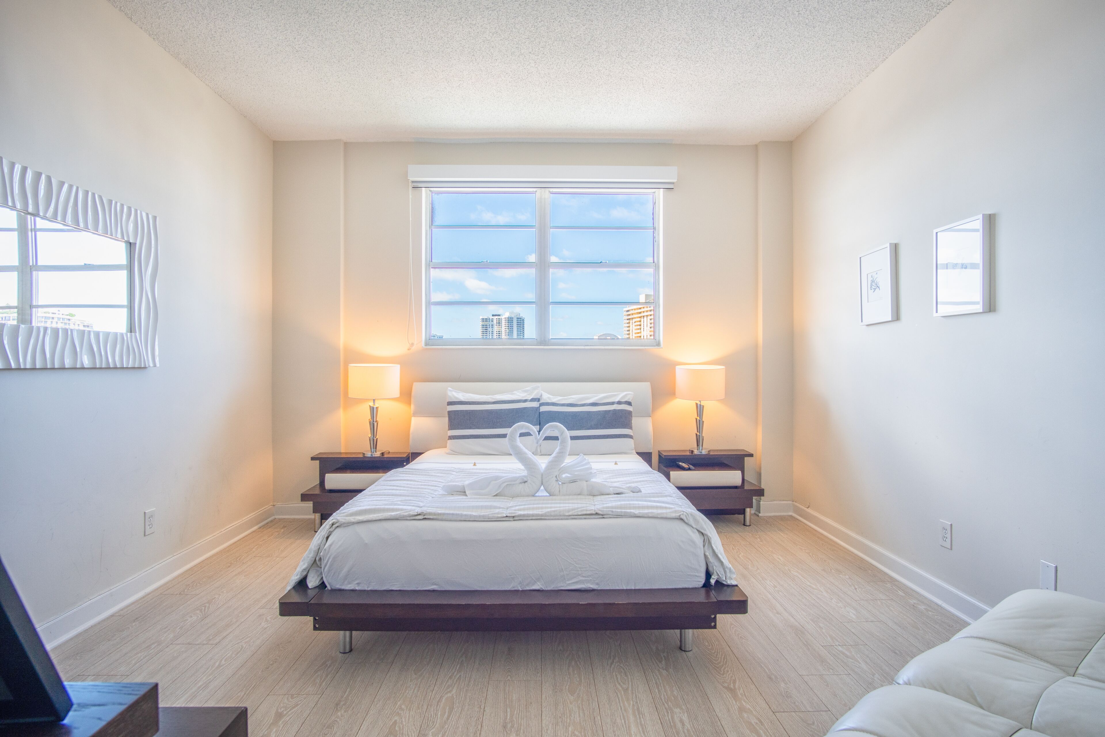 Una camera da letto moderna con un letto grande, due comodini, una finestra vista città e una parete bianca con due quadri incorniciati.