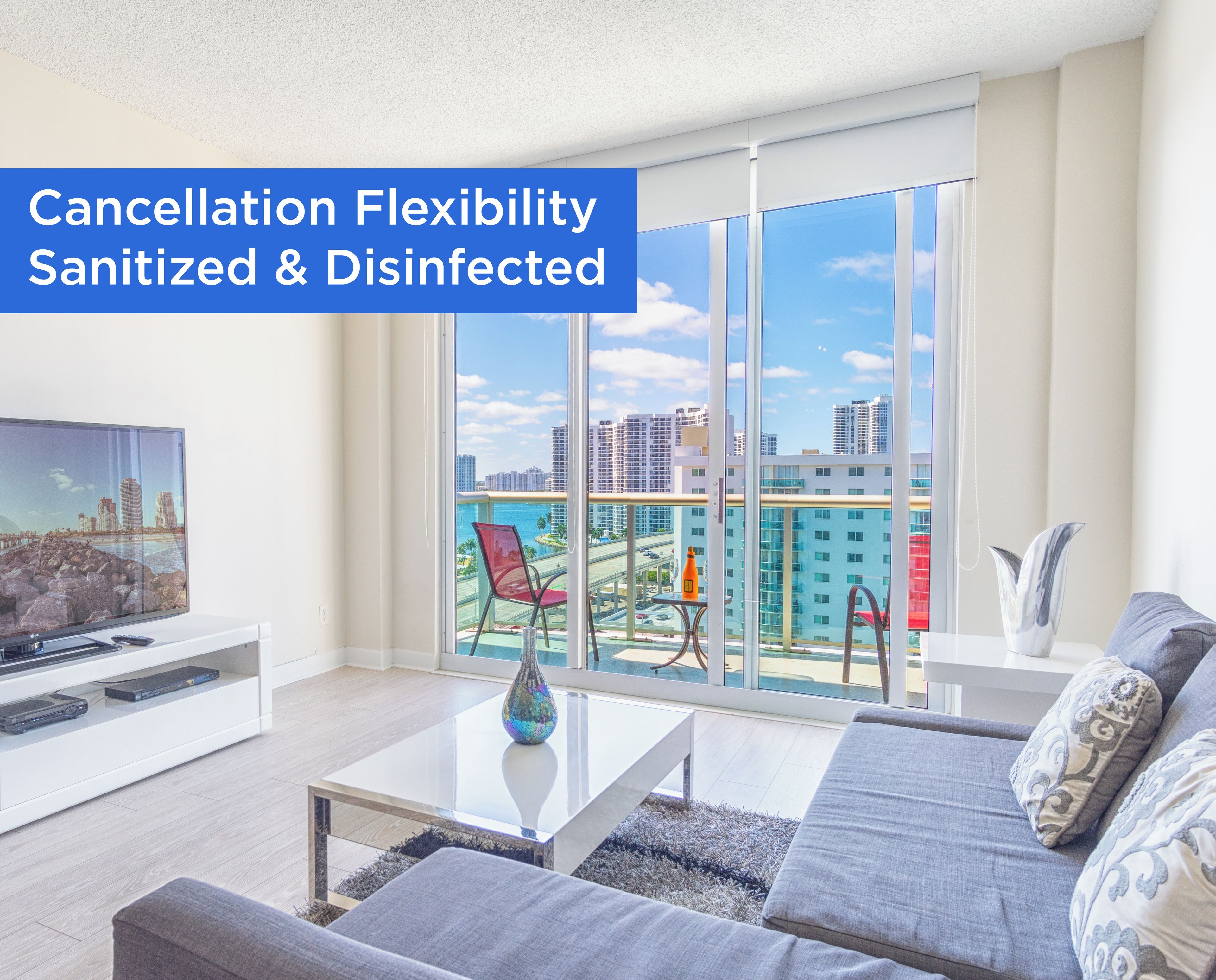 A modern living room with a large TV, comfortable seating, and a balcony with a city view.