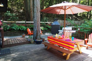 En träveranda med ett picknickbord, en färgglad duk och en grill.