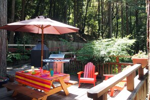 A wooden deck with a barbecue grill, picnic table, and outdoor seating.