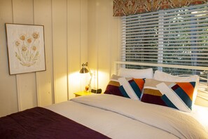A neatly made bed with a striped pillow, a bedside lamp, and a framed artwork on the wall.