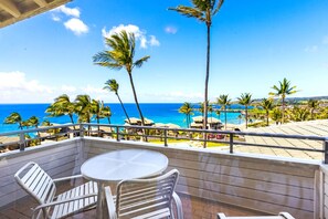 A balcony with a view of the ocean, palm trees, and a pool area.