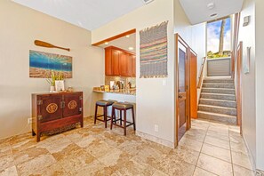 A spacious kitchen with a wooden cabinet, a painting, and a staircase leading to a balcony.