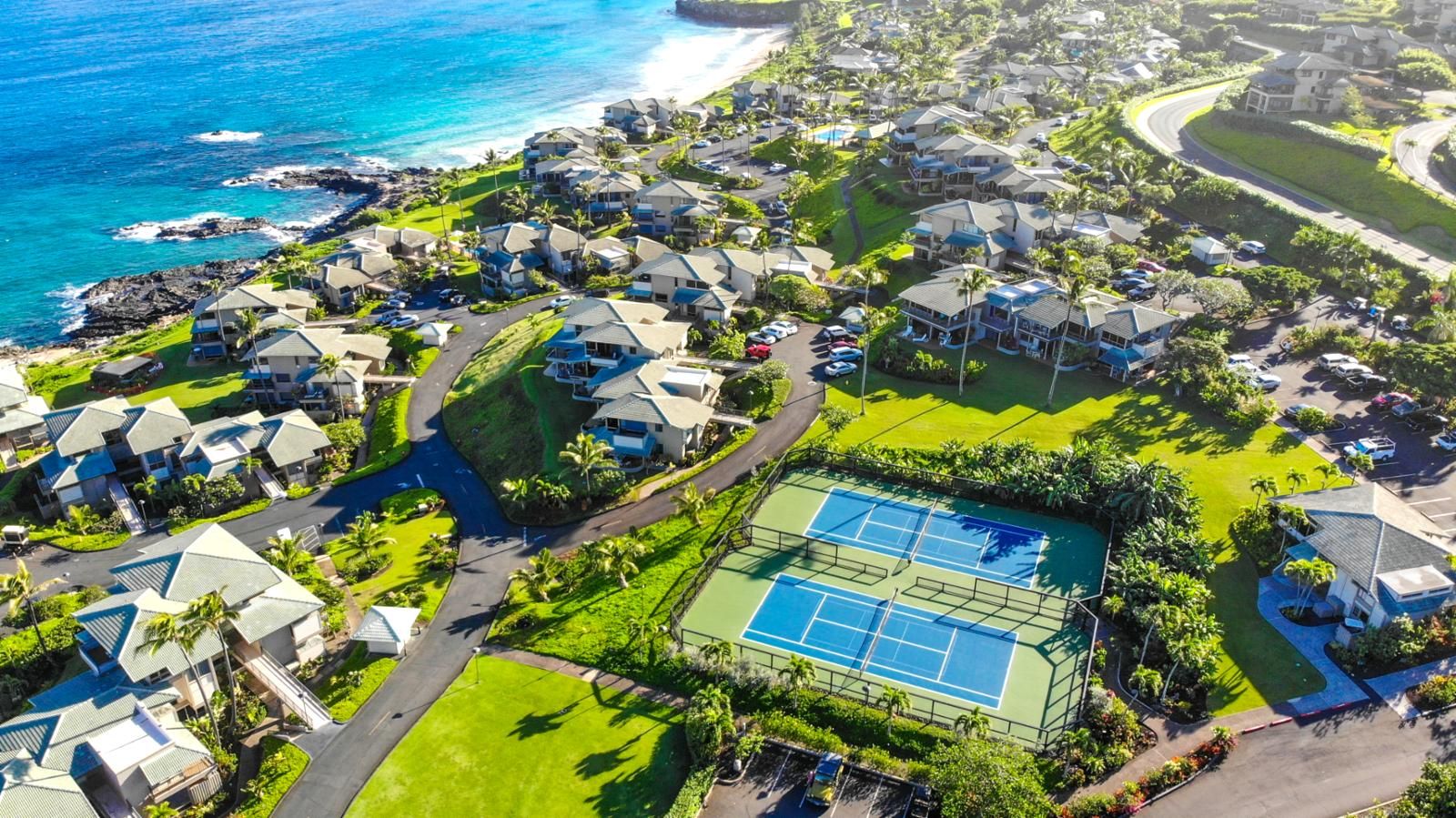 Luchtbeeld van een kustgebied met woonhuizen, een tennisbaan en een strand.