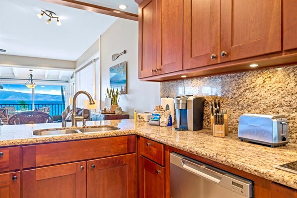 A kitchen with granite countertops, wooden cabinets, a coffee maker, a toaster, and a dishwasher.