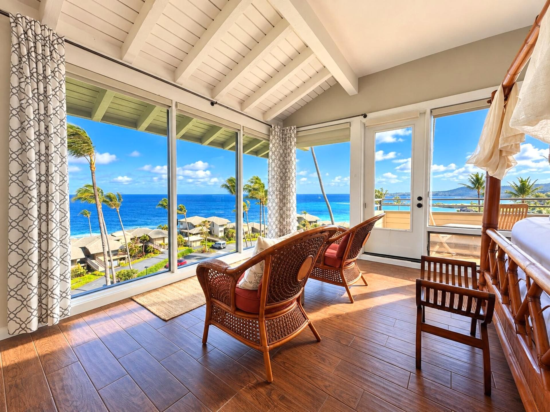 A room with a wooden floor, wicker furniture, and a large sliding glass door leading to a balcony with a view of the ocean and palm trees.