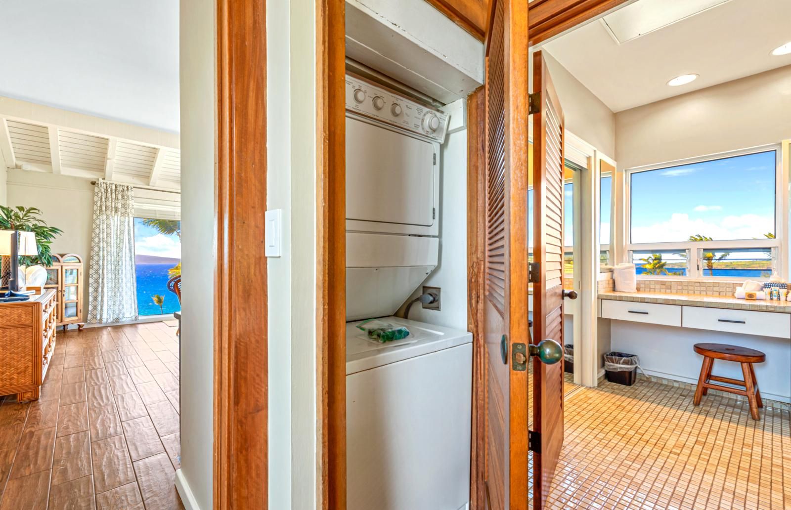 Een hotelkamer met een houten deur, uitzicht op zee, een keuken met een bar en een badkamer met een wasmachine.