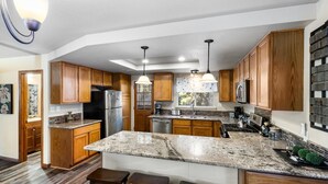Una cucina moderna con mobili in legno, piani in granito, elettrodomestici in acciaio inossidabile e luci a sospensione.