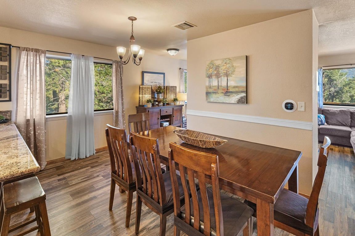 A dining area with a wooden table and chairs, a chandelier, and a painting on the wall.