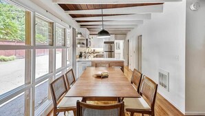 Una cocina amplia con una larga mesa de madera, armarios blancos y un ventanal con vistas a un jardín.