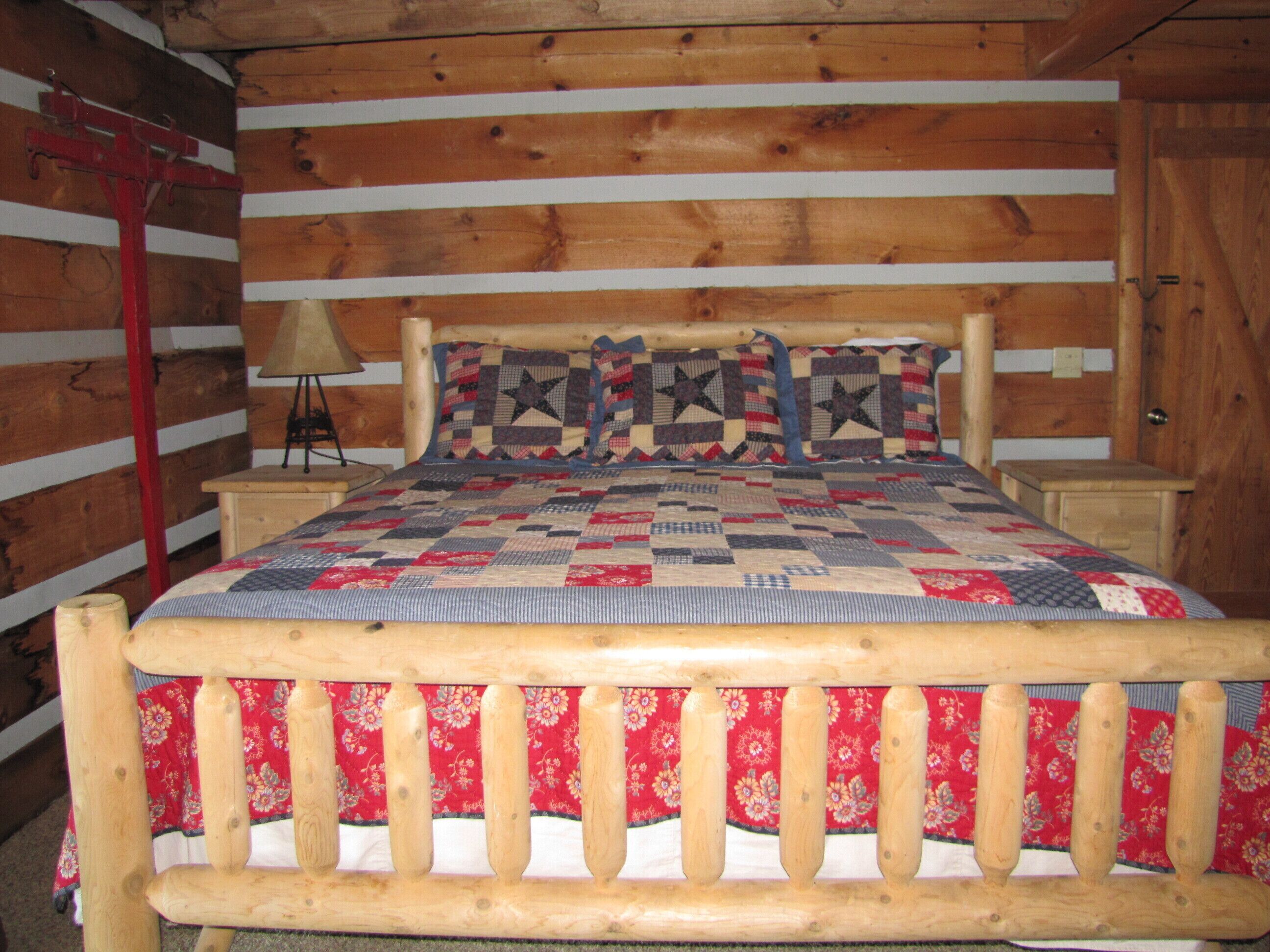 Quarto de cabana de madeira com uma cama, uma mesa de cabeceira, um abajur e uma cabeceira de madeira.