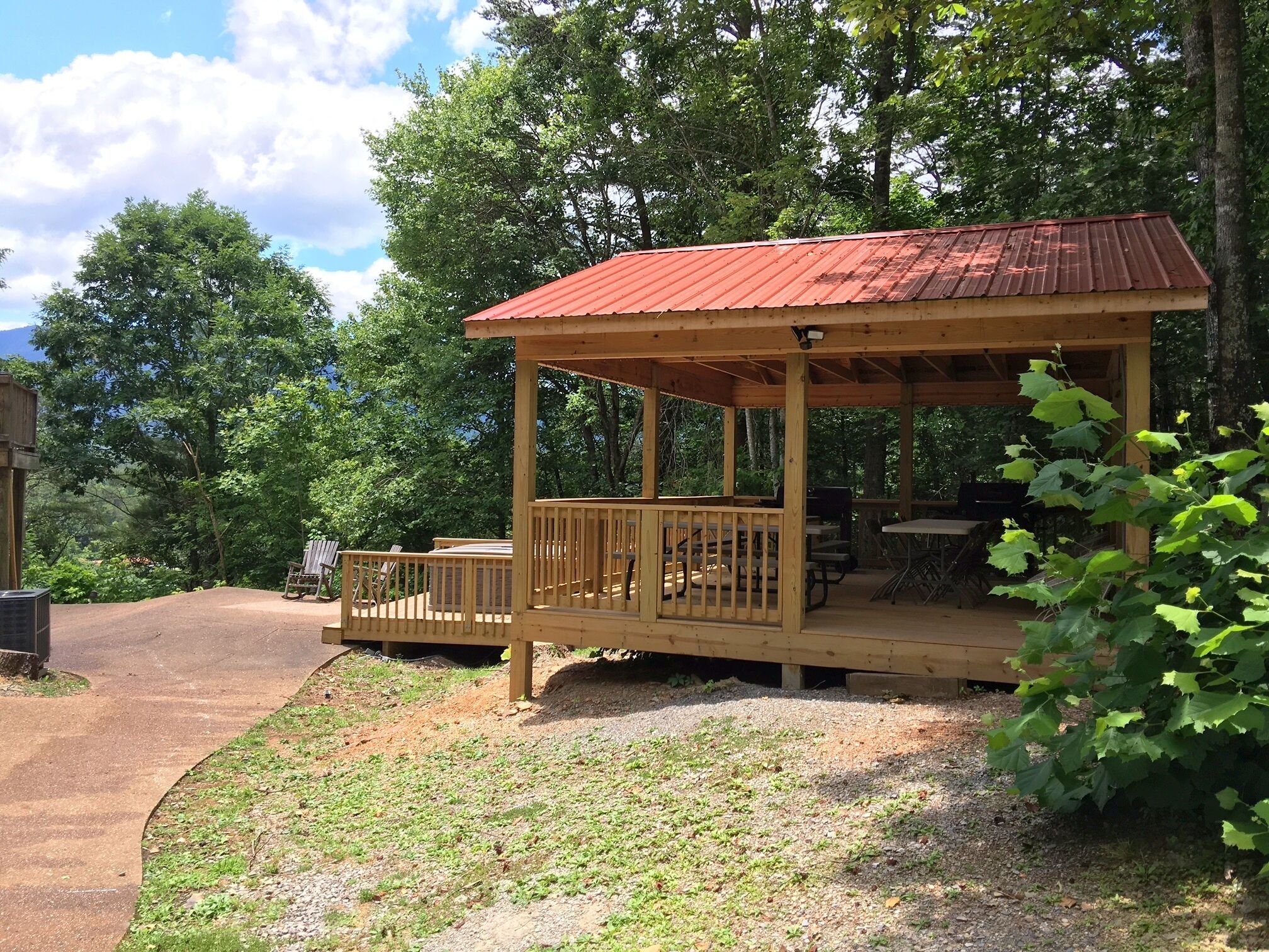 A wooden gazebo with a red roof, surrounded by trees and a gravel path.