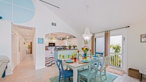 A modern kitchen with white cabinets, a central island, and a dining area with a white table and blue chairs. - Dream Catcher- Key West style beach house on North end. (Anna Maria)