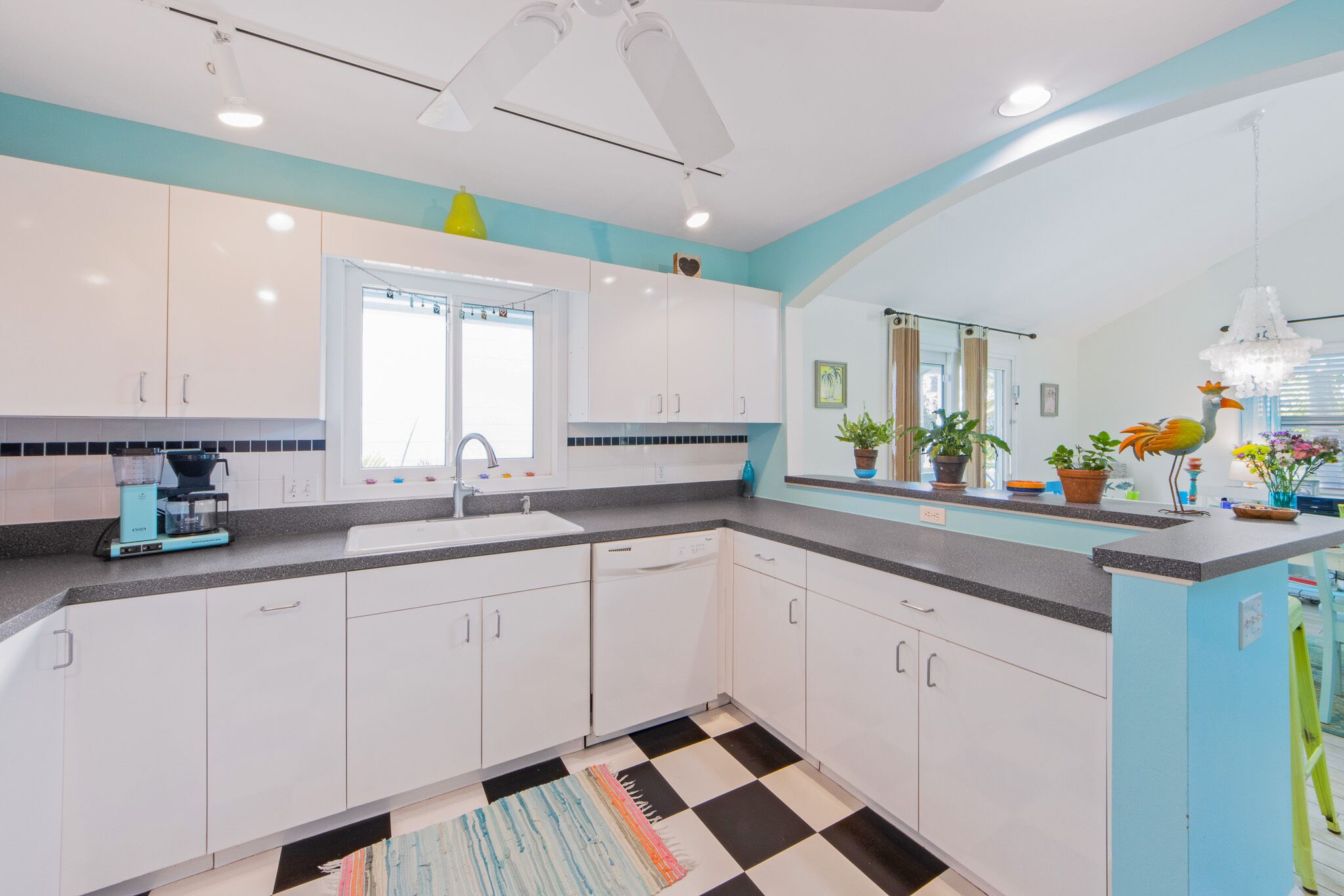 Una cocina moderna con armarios blancos, piso a cuadros blanco y negro, y una ventana con cortinas.