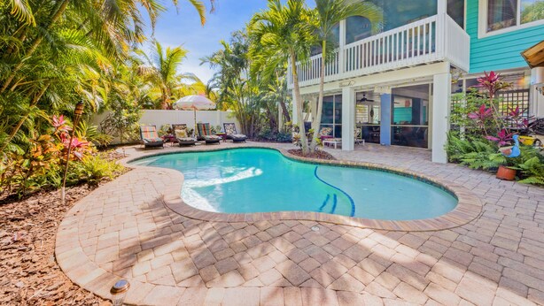 A swimming pool surrounded by palm trees and a two-story building with a balcony. - Dream Catcher- Key West style beach house on North end. (Anna Maria)