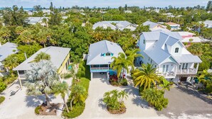 A coastal residential area with houses featuring light blue roofs and white walls, surrounded by lush greenery and palm trees. - Dream Catcher- Key West style beach house on North end. (Anna Maria)