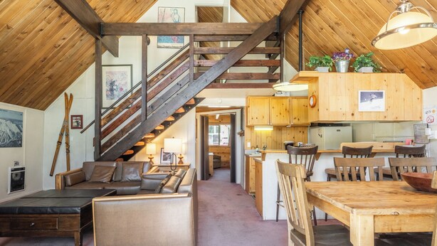 A spacious loft with a wooden staircase, a cozy seating area, and a kitchen with wooden cabinets. - Chalet #15, Charming Ski in/ Ski Out Steps to the (Mammoth Lakes)