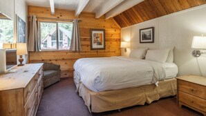 A cozy bedroom with a large bed, wooden walls, a dresser, and a window with curtains. - Chalet #15, Charming Ski in/ Ski Out Steps to the (Mammoth Lakes)