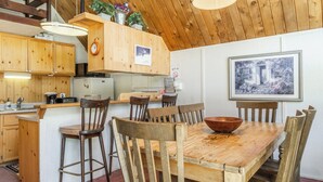 A rustic kitchen with wooden cabinets, a dining table with chairs, and a hanging light fixture. - Chalet #15, Charming Ski in/ Ski Out Steps to the (Mammoth Lakes)